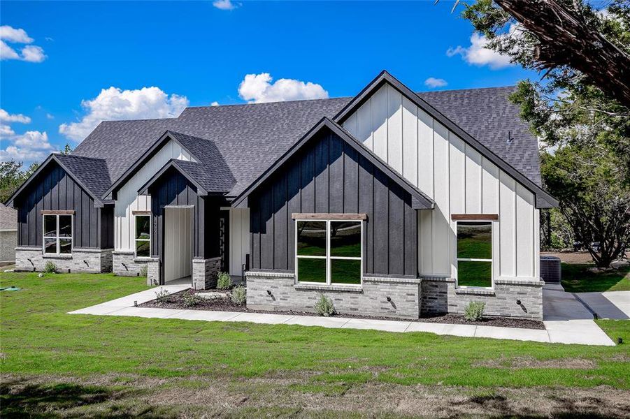 Modern farmhouse with board and batten siding, roof with shingles, and a front yard Modern farmhouse with board and batten siding, roof with shingles, and a front yard