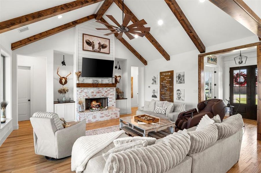 Living area with high vaulted ceiling, light hardwood wood flooring, beamed ceiling, a fireplace.