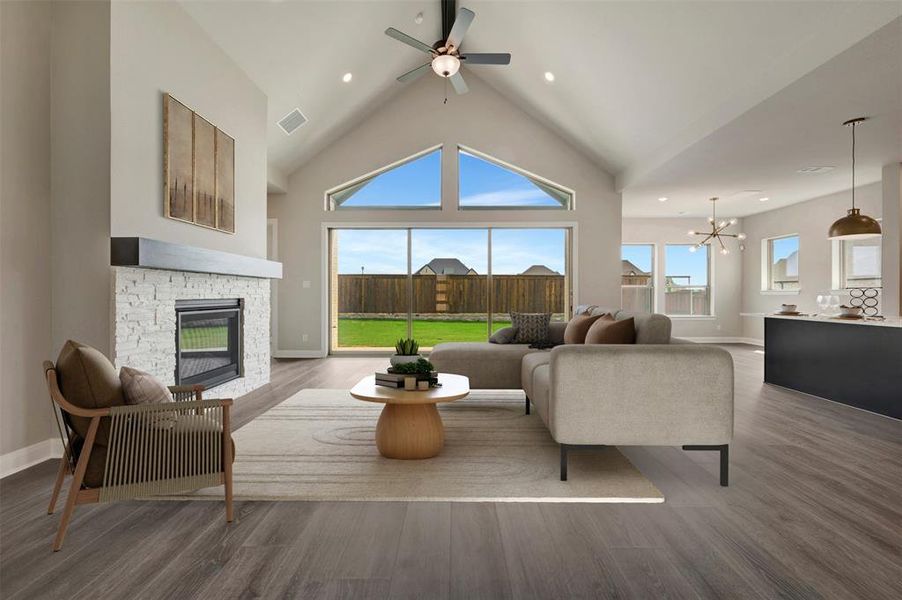 Vaulted ceiling living area featuring a stone-clad fireplace with a dark wood-finish mantel, wood-finish flooring, and expansive windows