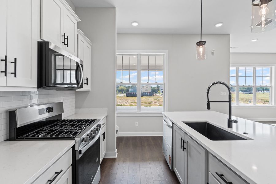 Kitchen with appliances with stainless steel finishes, hanging light fixtures, light stone counters, dark wood-type flooring, and backsplash Kitchen with appliances with stainless steel finishes, hanging light fixtures, light stone counters, dark wood-type flooring, and backsplash