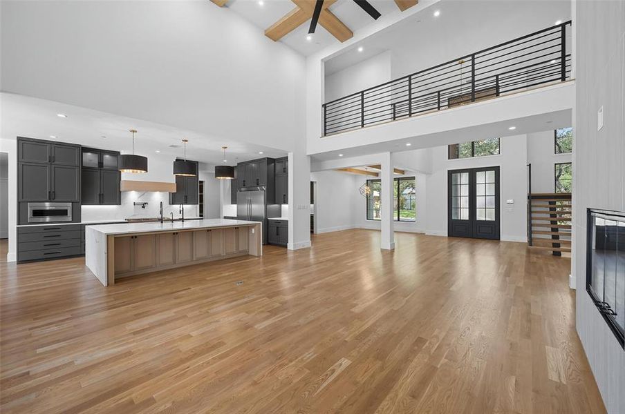 Example Open-concept living space featuring high ceilings, wood-finish flooring, and a modern kitchen with dark cabinetry and a large central island Example Open-concept living space featuring high ceilings, wood-finish flooring, and a modern kitchen with dark cabinetry and a large central island