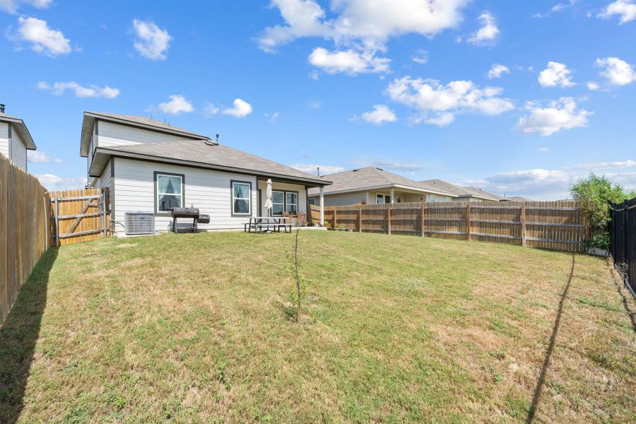 An expansive green lawn sits enclosed by privacy fencing behind the home.