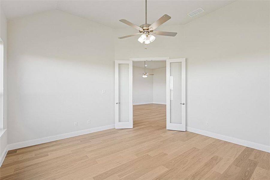 Unfurnished room featuring light wood finished floors, vaulted ceiling, a ceiling fan, and french doors