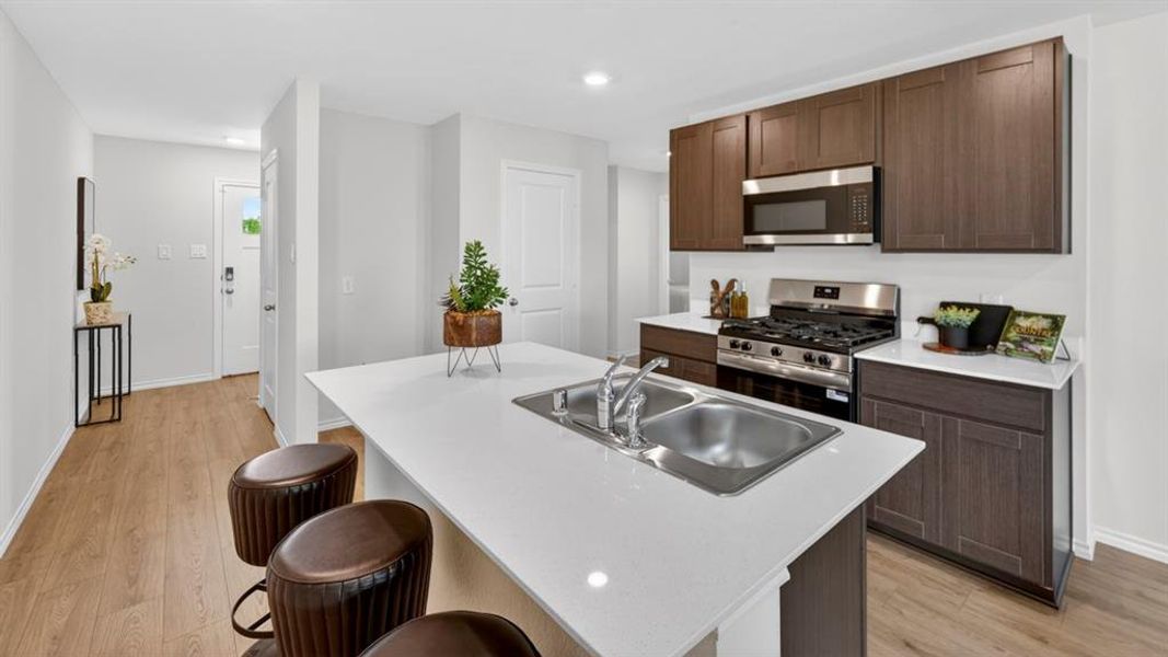 Modern kitchen featuring a large island with an undermount double-basin sink, white countertops, dark wood-finish cabinetry, stainless steel appliances, and wood-finish flooring Modern kitchen featuring a large island with an undermount double-basin sink, white countertops, dark wood-finish cabinetry, stainless steel appliances, and wood-finish flooring