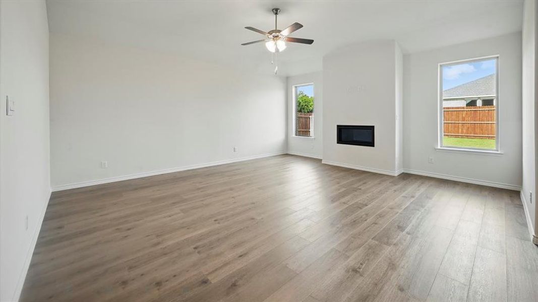 Unfurnished living room featuring light wood-style floors, a glass covered fireplace, and a ceiling fan