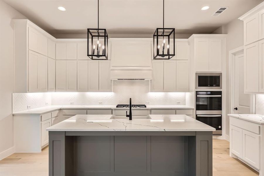 Kitchen with an island with sink, white cabinets, stainless steel appliances, and light stone counters