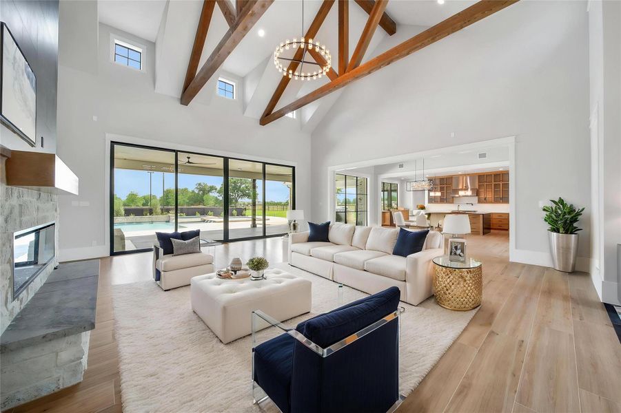 A grand welcome into the living area featuring high vaulted ceilings with exposed wooden beams, a modern electric fireplace, and large sliding glass doors that open to a patio and pool area. The open floor plan seamlessly connects to a contemporary kitchen, providing a bright and airy ambiance. A grand welcome into the living area featuring high vaulted ceilings with exposed wooden beams, a modern electric fireplace, and large sliding glass doors that open to a patio and pool area. The open floor plan seamlessly connects to a contemporary kitchen, providing a bright and airy ambiance.