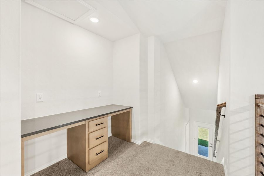 Loft office area with built-in wood desk, gray countertop, and carpet flooring near staircase opening Loft office area with built-in wood desk, gray countertop, and carpet flooring near staircase opening