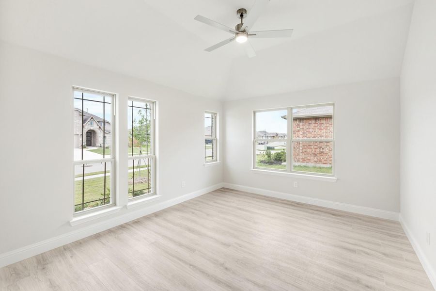 Empty room with light wood floors, ceiling fan, and multiple windows with neighborhood views