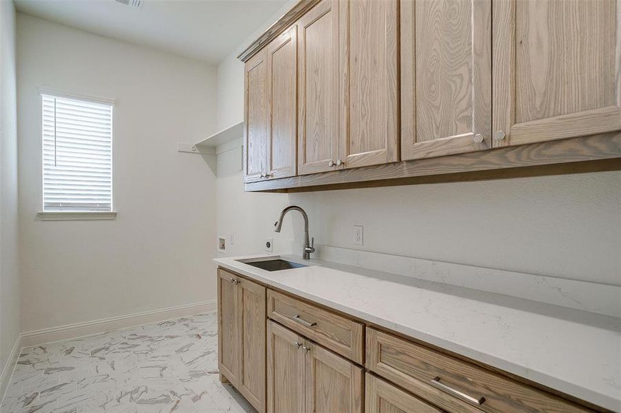 Laundry room with custom built natural stain cabinets and drawers, Quartz countertops and hookup for full size W/D, and sink.