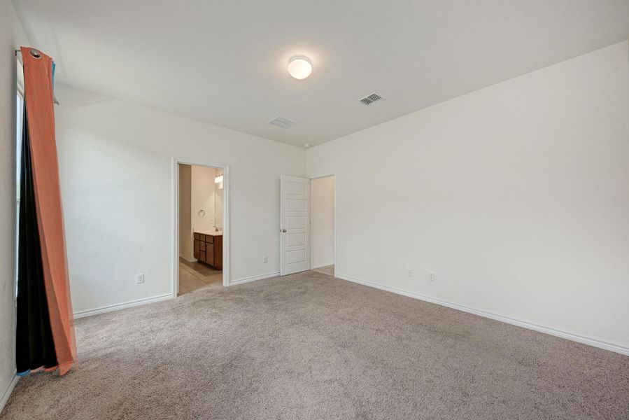 A spacious, neutral-toned room featuring plush carpeting and easy access to an adjacent bathroom.
