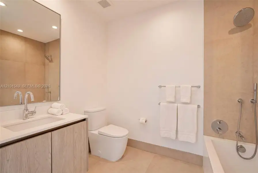Bathroom featuring wood-finish cabinetry, a white rectangular sink, large-format tile surround, chrome wall-mounted fixtures, and a glass-enclosed soaking tub