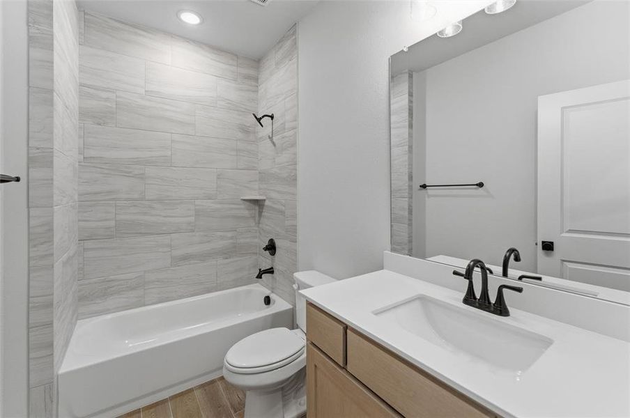 Bathroom featuring a white bathtub, light-toned rectangular wall tiling, wood-finish flooring, a vanity with light wood cabinetry, and a white countertop with an integrated sink