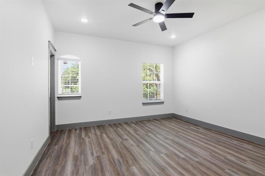 Spacious interior room featuring wood-finish flooring, two windows with blinds, a contemporary ceiling fan, and recessed lighting