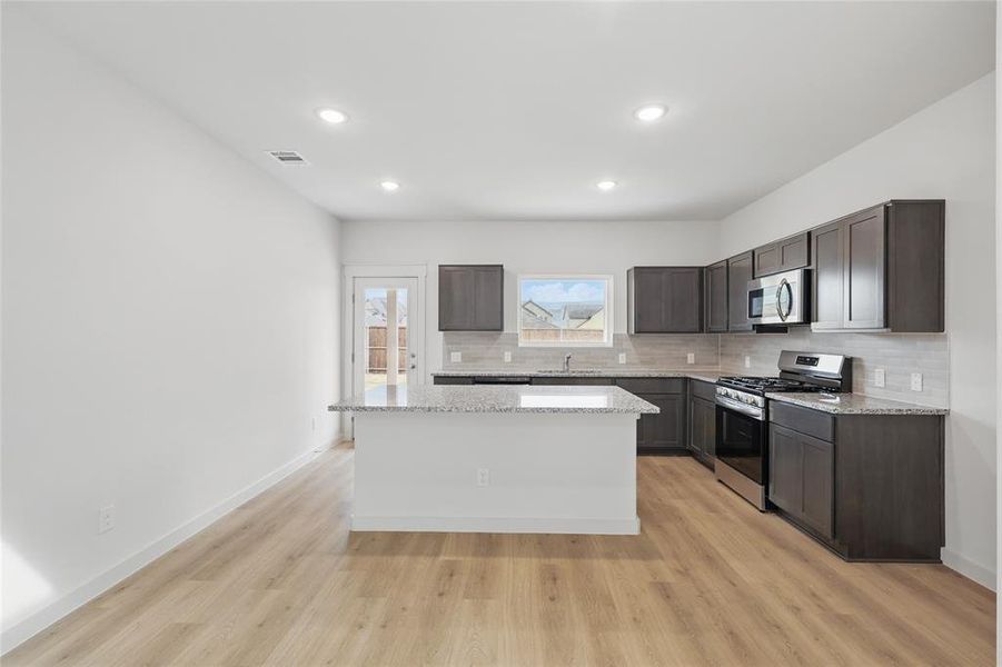 Kitchen featuring stainless steel appliances, dark wood finish cabinets, light stone countertops, light wood-style flooring, and recessed lighting