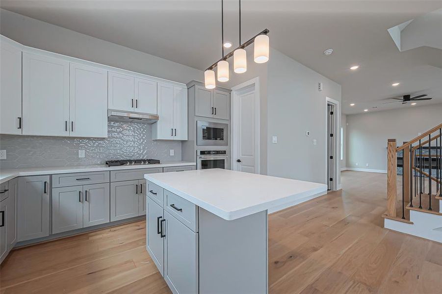 Experience culinary elegance in this modern kitchen, featuring sleek white and gray cabinetry, quartz countertops, and a chic backsplash. Enjoy stainless steel appliances, abundant natural light from a large window, and stylish pendant lighting. Perfect for cooking and entertaining.