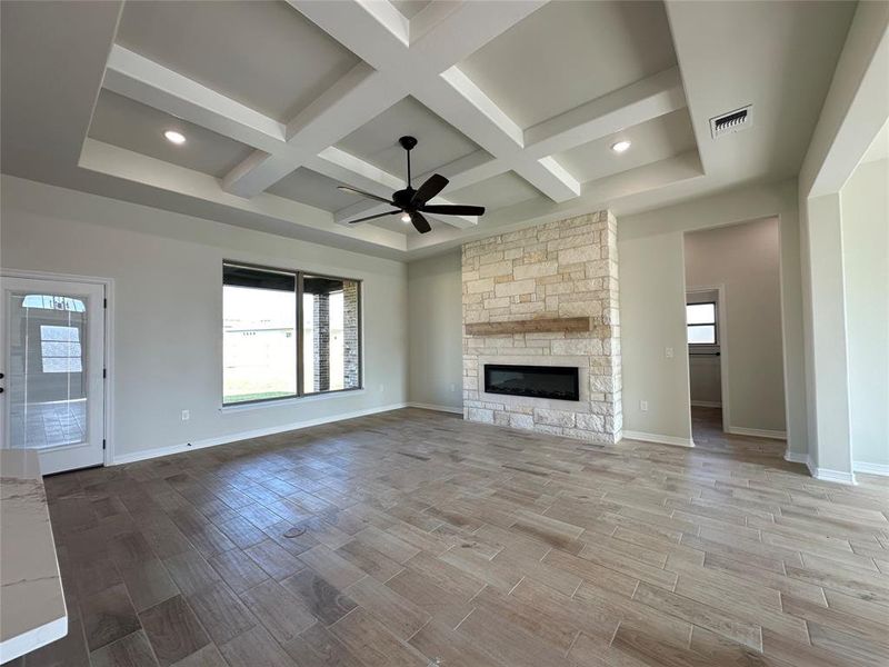 Unfurnished living room featuring plenty of natural light, wood tiled floors, a stone fireplace, coffered ceiling, and beam ceiling