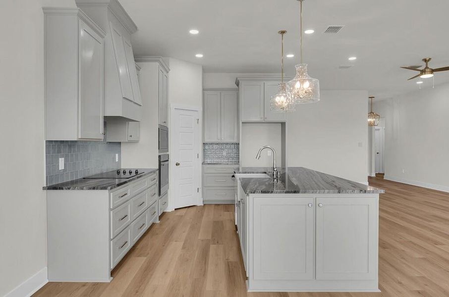 Kitchen featuring dark stone counters, hanging light fixtures, a center island with sink, light wood-style floors, and recessed lighting
