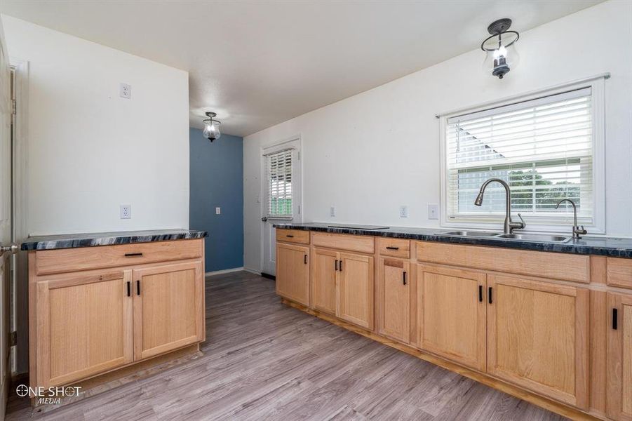 Kitchen with sink, kitchen peninsula, light brown cabinets, light wood-type flooring, and dark stone countertops