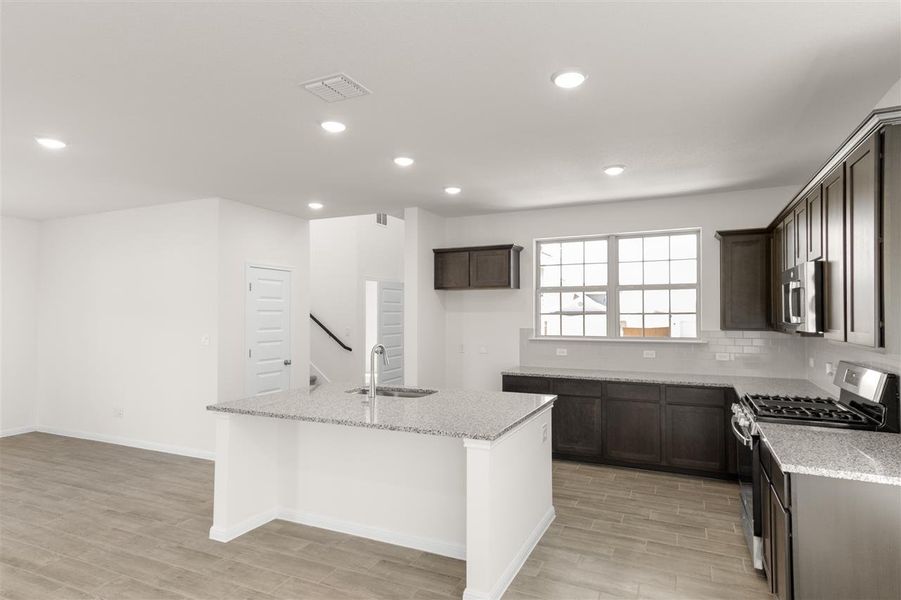 Kitchen with visible vents, a kitchen island with sink, stainless steel appliances, a sink, and light stone counters