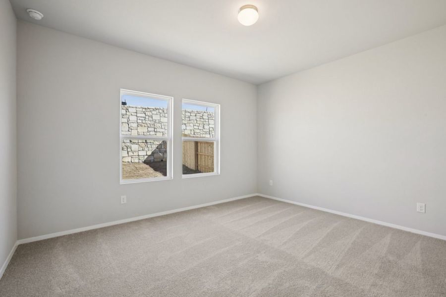 Image of a primary bedroom with light grey walls, tan carpeting, windows and white trim