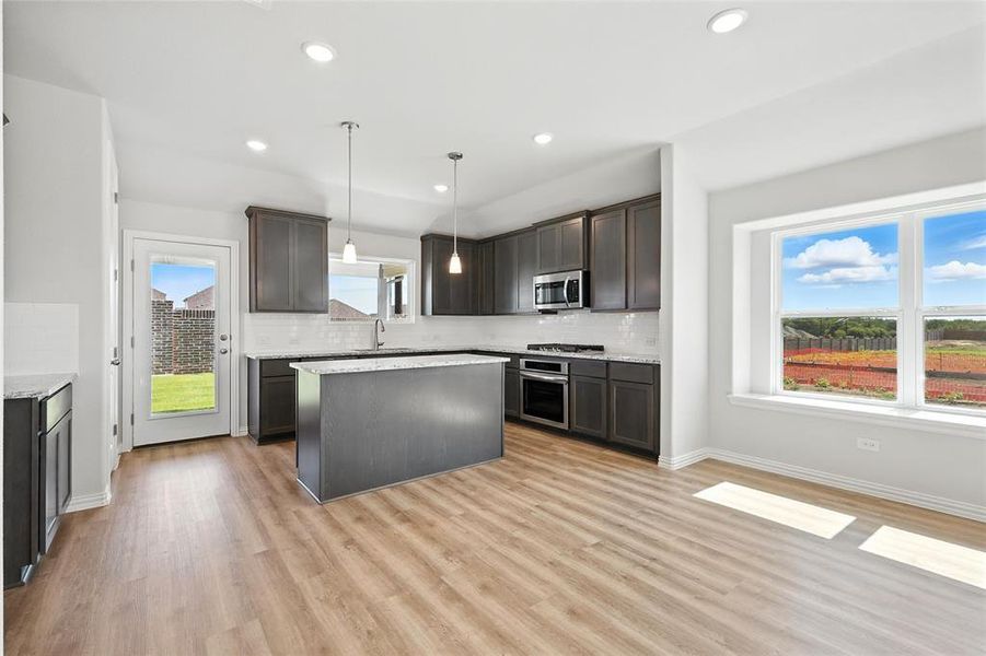 Kitchen featuring appliances with stainless steel finishes, backsplash, a center island, light wood-style floors, and dark brown cabinetry Kitchen featuring appliances with stainless steel finishes, backsplash, a center island, light wood-style floors, and dark brown cabinetry