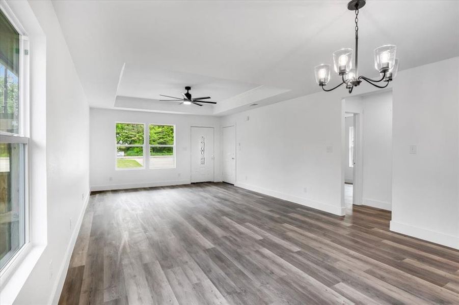 Spare room with dark hardwood / wood-style floors, a raised ceiling, and ceiling fan with notable chandelier