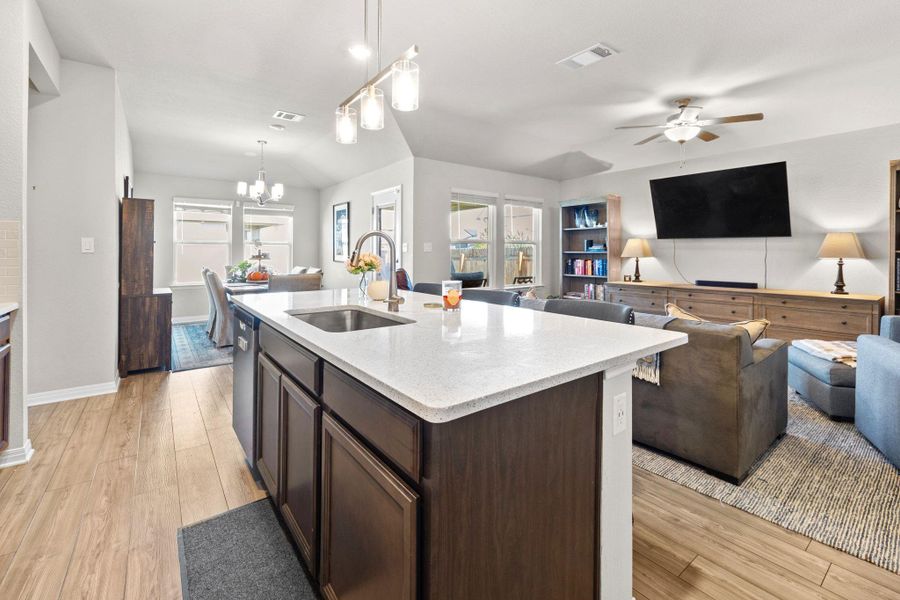 Kitchen featuring dark brown cabinetry, light wood finished floors, open floor plan, and light stone counters Kitchen featuring dark brown cabinetry, light wood finished floors, open floor plan, and light stone counters