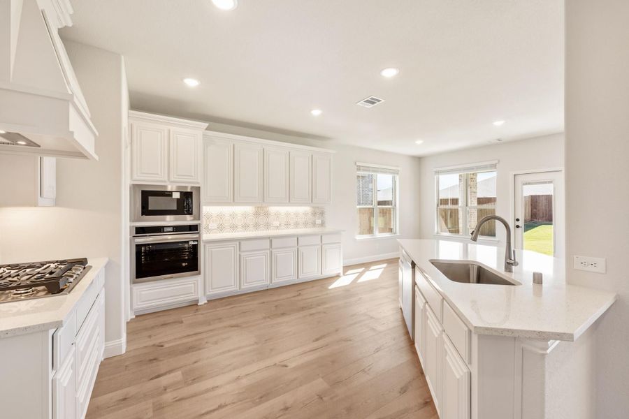 Kitchen with white cabinets, quartz island, stainless steel appliances, and light hardwood floors