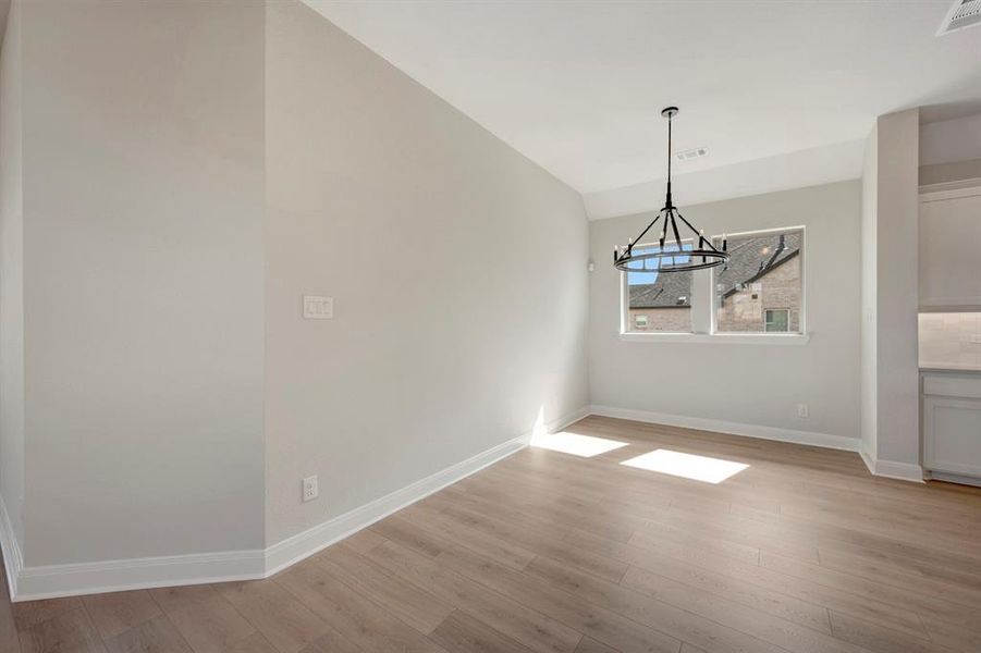 Unfurnished dining area with vaulted ceiling, light wood-type flooring, and suspended lighting