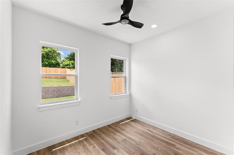 Room featuring wood-finish flooring, white walls, two windows, a ceiling fan, and recessed lighting