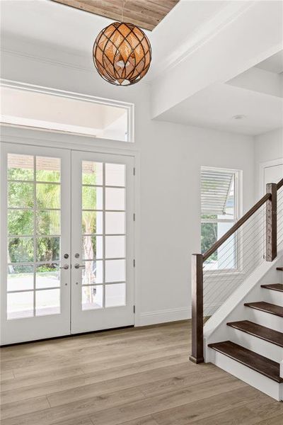 Alternate foyer view highlighting the double glass entry doors, decorative light fixture, and the adjacent staircase with dark wood treads and white risers.