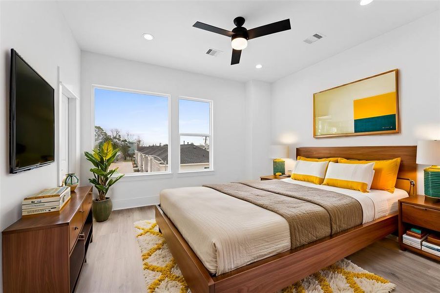 This is a bright, spacious virtually staged room featuring large windows with a view, light wood flooring, and a modern ceiling fan. The walls are painted white, enhancing the natural light.