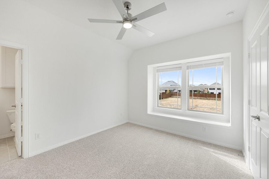 Empty bedroom with vaulted ceiling, ceiling fan, carpet flooring, and attached bathroom