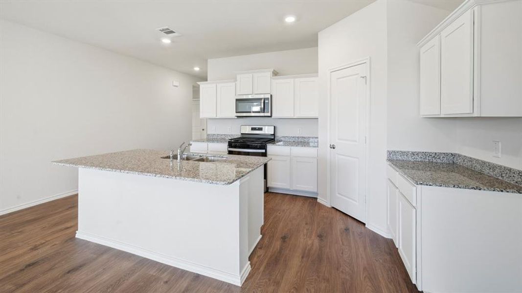 Kitchen featuring white cabinets, light stone counters, an island with sink, and recessed lighting