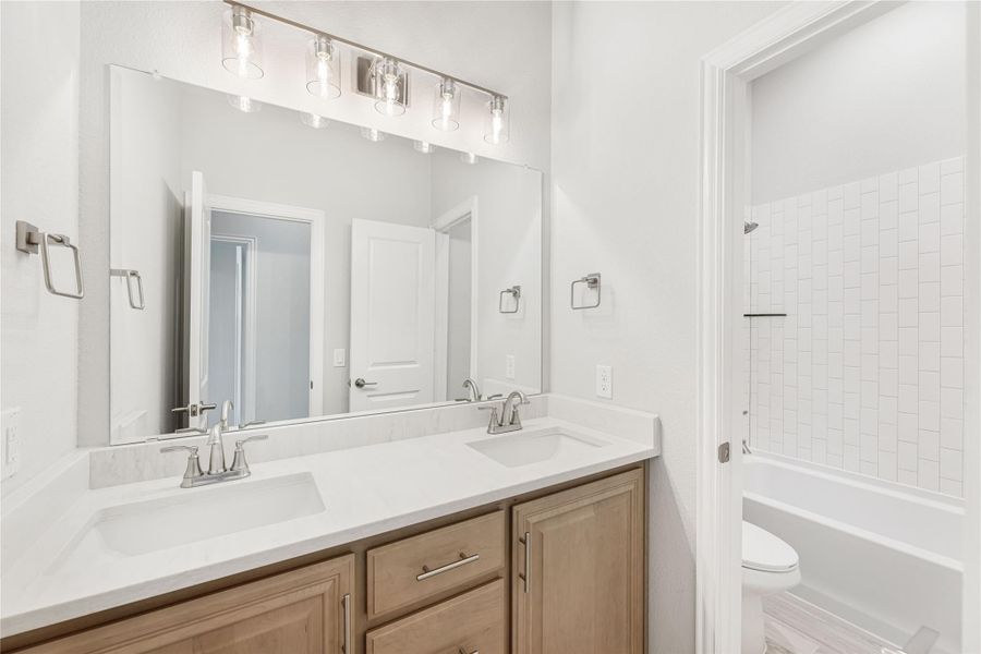 Bathroom with double sink vanity, wood cabinets, large mirror, and tiled shower-tub combo