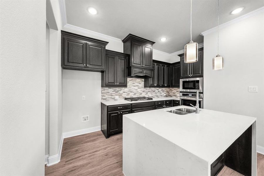 Kitchen with crown molding, light wood-style flooring, light countertops, stainless steel appliances, and tasteful backsplash Kitchen with crown molding, light wood-style flooring, light countertops, stainless steel appliances, and tasteful backsplash