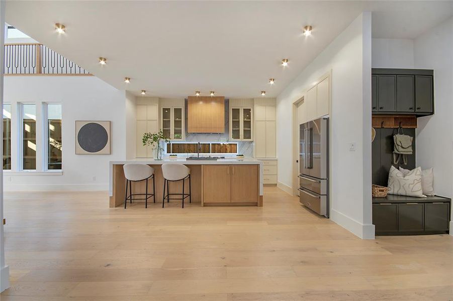 Kitchen featuring a kitchen breakfast bar, backsplash, light wood-style floors, high end refrigerator, and glass insert cabinets Kitchen featuring a kitchen breakfast bar, backsplash, light wood-style floors, high end refrigerator, and glass insert cabinets