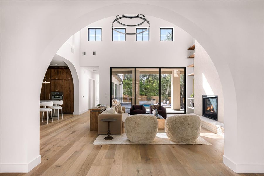 An elegant arched opening reveals soaring double-height ceilings, a fireplace, and warm hardwood floors.