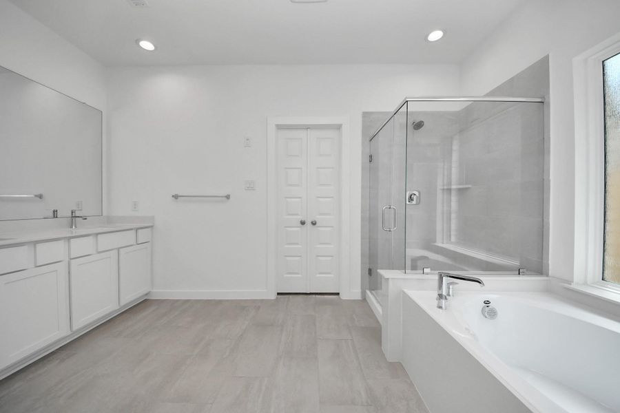 Escape to a spa-like oasis in this primary bathroom. Enjoy a walk-in shower with tile surround, a separate garden tub with custom detailing, and an elegant vanity featuring light countertops, modern hardware, and beautiful vanity lights. Experience luxury and relaxation in every detail. Sample photo of completed home with similar floor plan. Actual colors and selections may vary. Escape to a spa-like oasis in this primary bathroom. Enjoy a walk-in shower with tile surround, a separate garden tub with custom detailing, and an elegant vanity featuring light countertops, modern hardware, and beautiful vanity lights. Experience luxury and relaxation in every detail. Sample photo of completed home with similar floor plan. Actual colors and selections may vary.