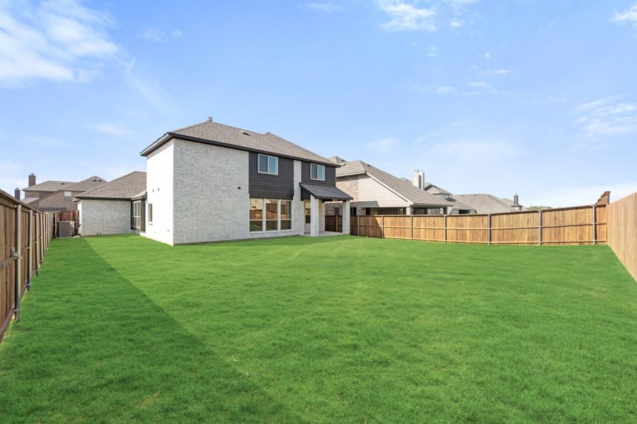 Two-story brick home with large grassy backyard, covered patio, and wood privacy fence