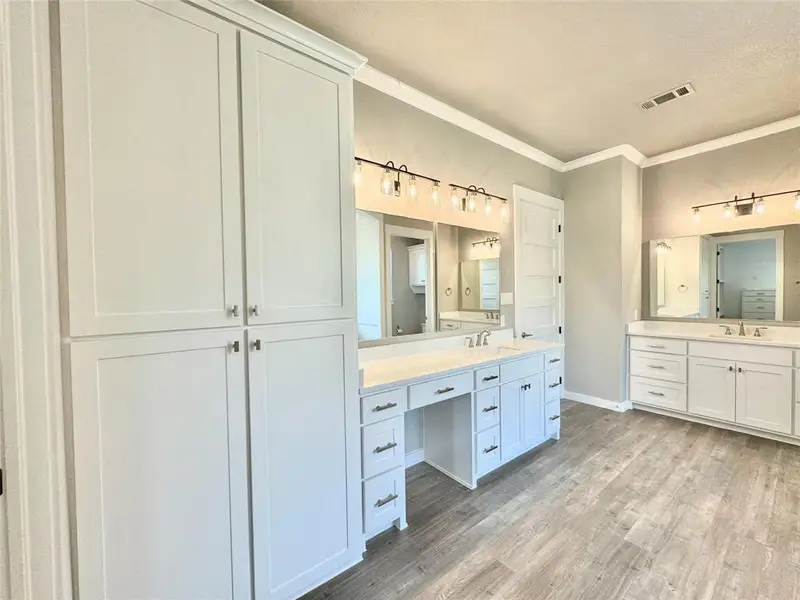 Full bathroom with crown molding, two vanities, wood finished floors, baseboards, and a textured ceiling