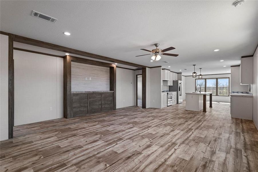 Unfurnished living room with light wood-type flooring, a ceiling fan, and suspended lighting