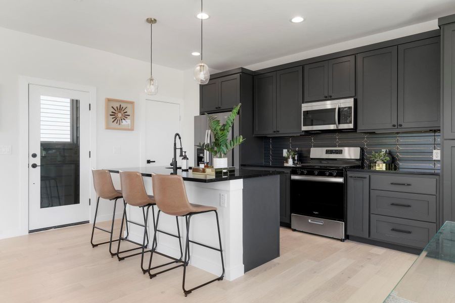 Kitchen with backsplash, stainless steel appliances, hanging light fixtures, a breakfast bar area, and light wood finished floors