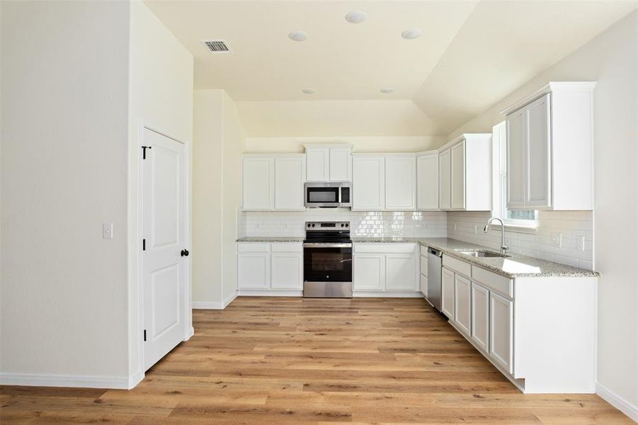 Kitchen featuring stainless steel appliances, backsplash, granite countertops, and white cabinets Kitchen featuring stainless steel appliances, backsplash, granite countertops, and white cabinets