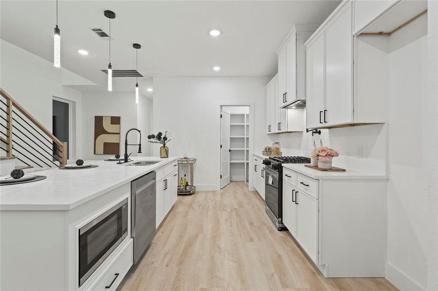 Kitchen with white cabinetry, decorative light fixtures, appliances with stainless steel finishes, light wood finished floors, and recessed lighting Kitchen with white cabinetry, decorative light fixtures, appliances with stainless steel finishes, light wood finished floors, and recessed lighting