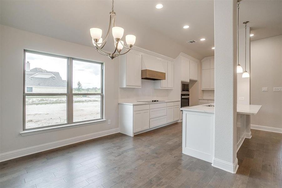 Kitchen featuring dark wood-type flooring, white cabinetry, stainless steel appliances, and premium range hood