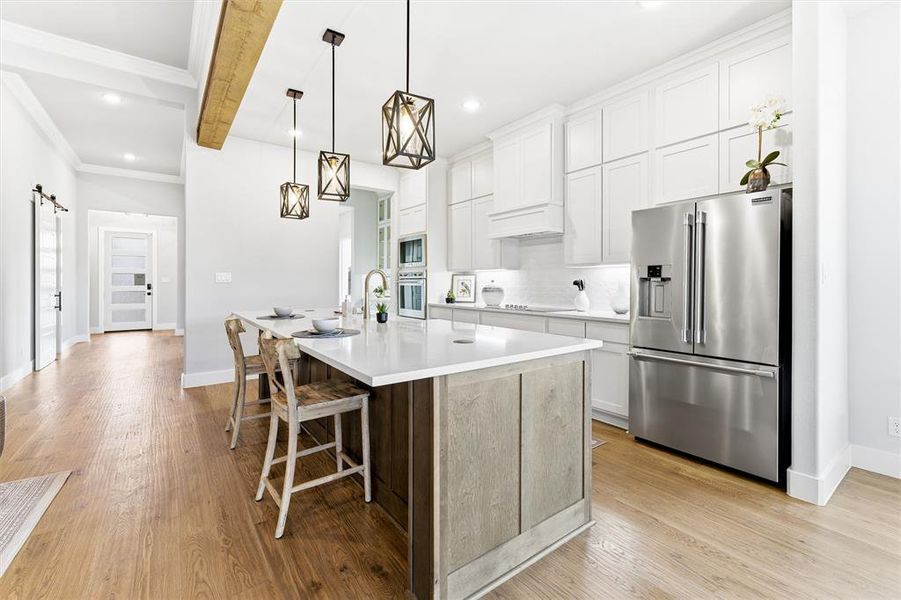 Kitchen featuring a barn door, stainless steel appliances, white cabinetry, a kitchen breakfast bar, and crown molding