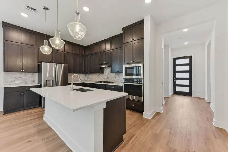 Contemporary kitchen featuring dark wood cabinetry, white countertops, stainless steel appliances, and wood-finish flooring