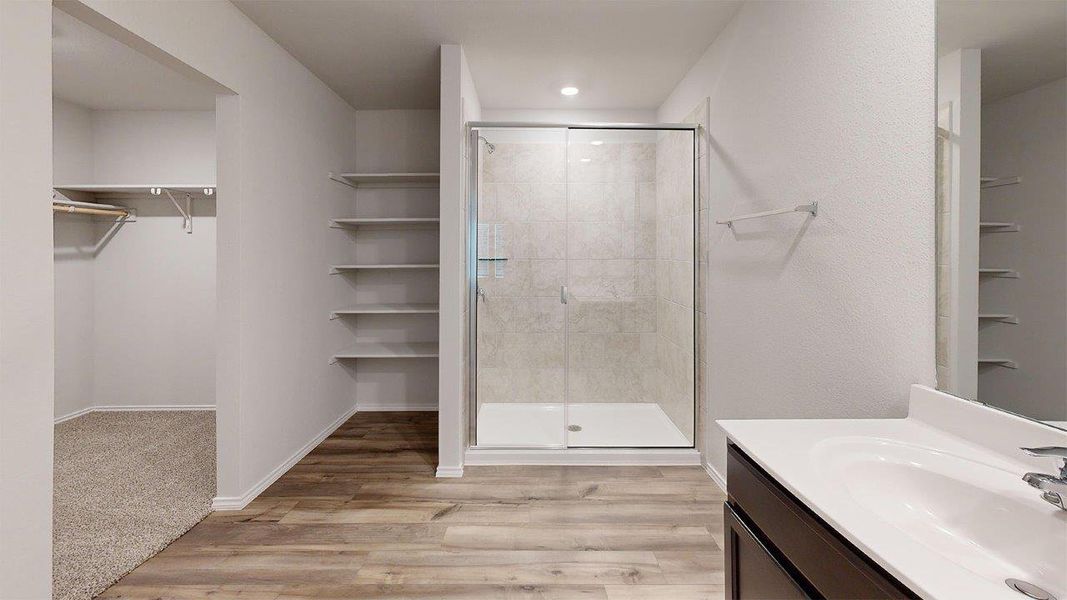 Glass-enclosed shower with tiled surround, wood-finish flooring, built-in shelving, and a vanity with a white countertop Glass-enclosed shower with tiled surround, wood-finish flooring, built-in shelving, and a vanity with a white countertop